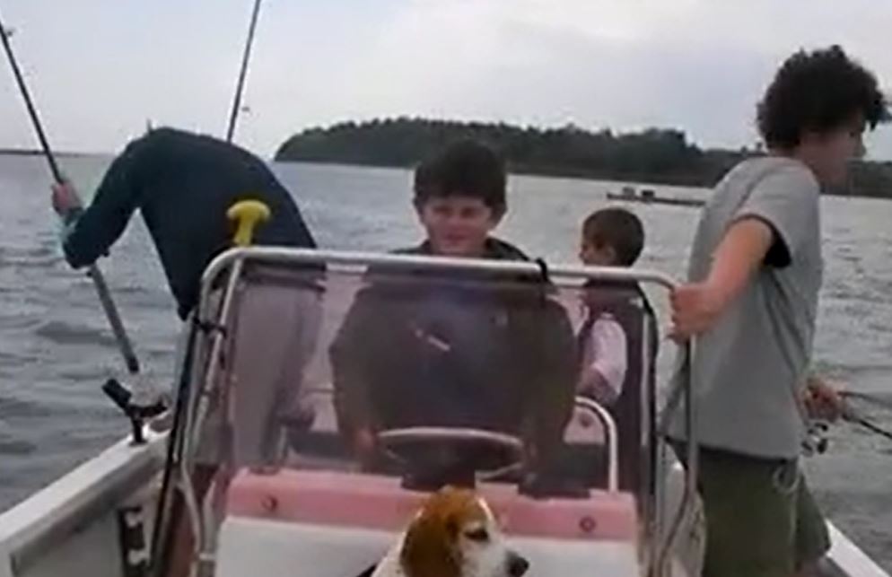 A child steers a motorboat off the coast of Maine. His family holds fishing rods over the sides of the boat.